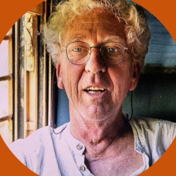 Portrait de Pompon, cheveux blancs bouclés et lunettes, en chemise claire, qui sourit en parlant.